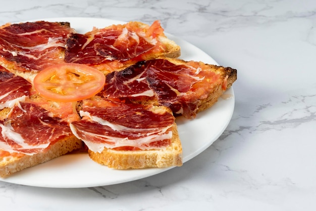 Plato de tostadas con delicioso jamón ibérico con una rodaja de tomate Plato típico español