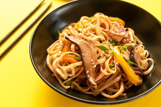 Un plato tradicional asiático fideos udon chinos en un plato negro sobre un fondo amarillo