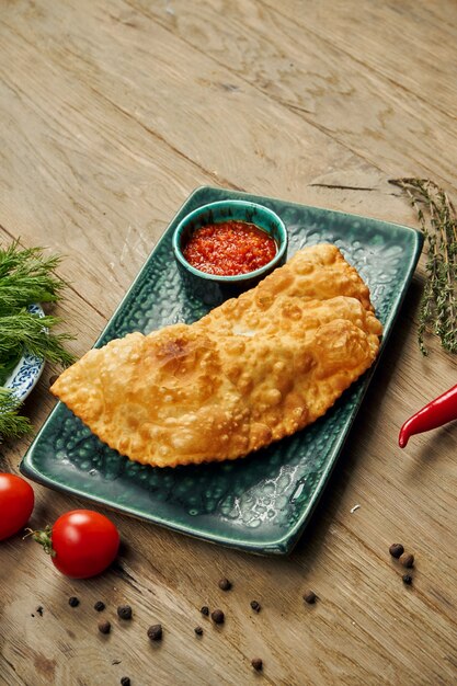 El plato tradicional del Cáucaso es Cheburek, un aceite de pastel frito con diferentes rellenos, principalmente carne o queso en un plato azul.