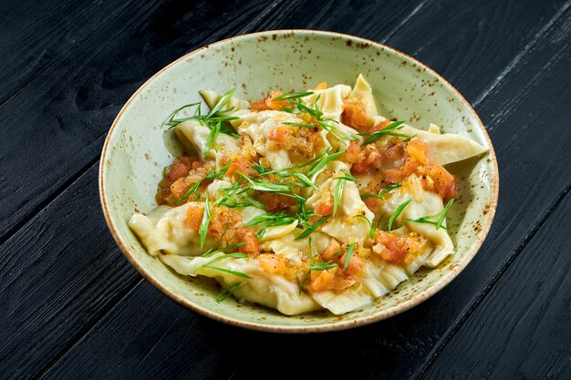 Plato tradicional de la cocina israelí - kreplach de pollo con salsa de tomate y cebollas verdes en un plato sobre un fondo de madera negra. Comida de restaurante. Bolas de masa con diferentes rellenos