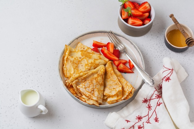 Plato tradicional para fiesta Maslenitsa. Tortitas de crepes finas con miel, fresa fresca e ingredientes para hacer el desayuno. Vista superior.