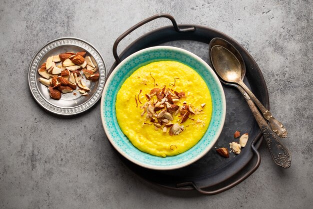 Plato tradicional indio Kheer, pudín de leche de arroz dulce con almendras y azafrán en cuenco de cerámica azul con cucharas sobre fondo rústico de piedra, vista superior. Comida de postre de la cocina india.