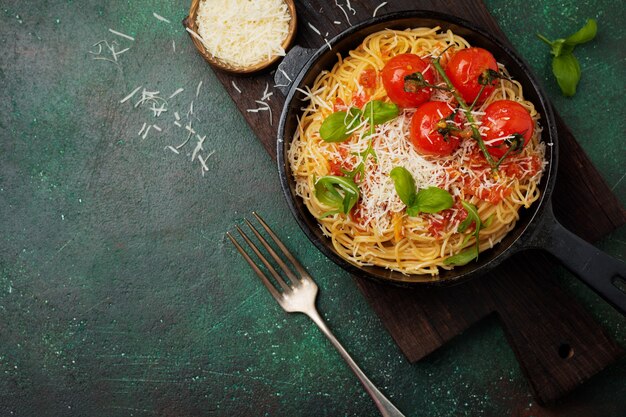 Plato tradicional italiano de espaguetis con salsa de tomate y queso parmesano en una sartén de hierro sobre la superficie de hormigón viejo oscuro. Enfoque selectivo. Vista superior.