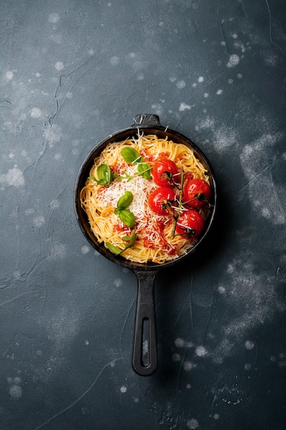 Plato tradicional italiano de espaguetis con salsa de tomate y queso parmesano en una sartén de hierro sobre la superficie de hormigón viejo oscuro. Enfoque selectivo. Vista superior.