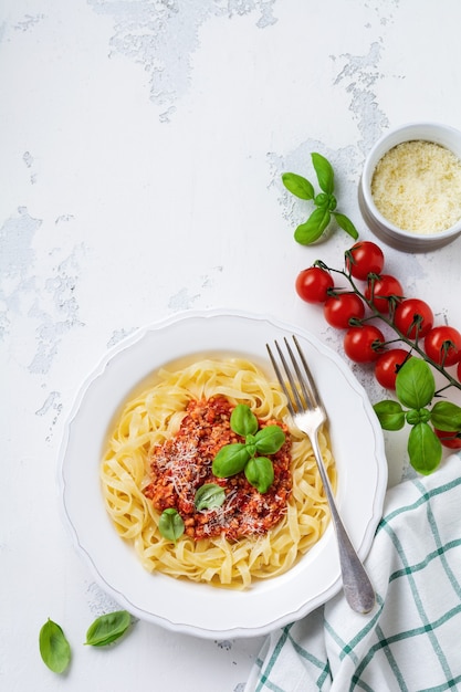 Plato tradicional italiano de pasta fettuccine con salsa boloñesa, albahaca y queso parmesano en una placa blanca sobre un fondo de madera clara