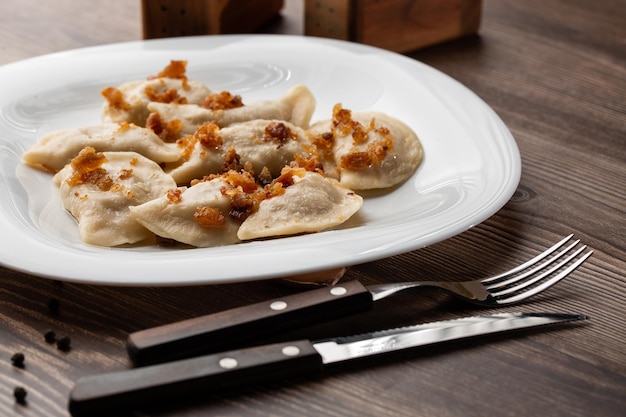 Plato tradicional ucraniano vareniki servido en un bol con chicharrones y crema agria Vista de cerca de la comida tradicional ucraniana