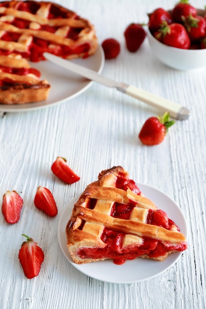 Plato con un trozo de delicioso pastel de fresas en una mesa de madera blanca