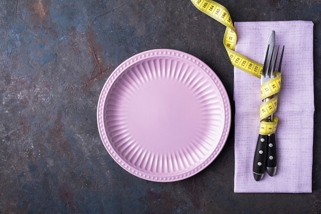 Plato vacío, cuchillo y tenedor con cinta métrica. Concepto de comida de dieta. Vista superior.