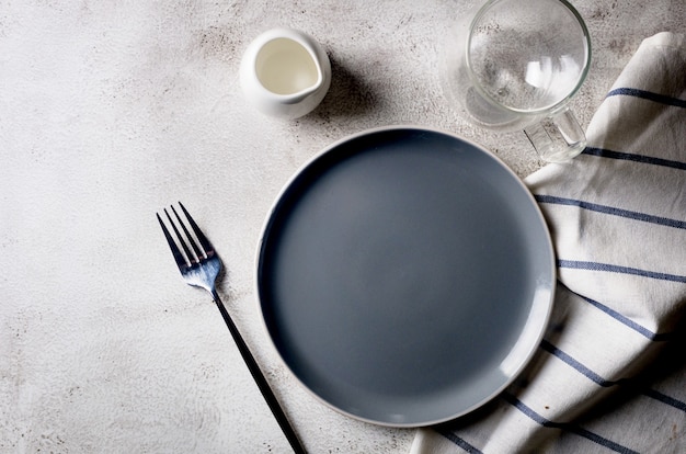 Plato vacío elegante, cubiertos, taza de café para comer por la mañana, fondo de mesa de luz, vista superior.