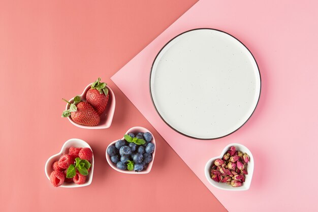 Plato vacío y platos pequeños en forma de corazones con fresas frescas frambuesas arándanos