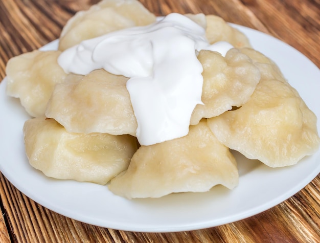 Plato con varenyky hervido y crema agria sobre mesa de madera Cerrar