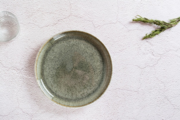 Plato verde de cerámica vacío un vaso de agua y ramas de romero sobre un fondo gris Vista superior Concepto ecológico