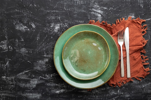 Plato verde vacío servido con cuchillo, tenedor y servilleta de mesa. Placa de plantilla de maqueta para cena de lujo con espacio de copia en la vista superior de la mesa de hormigón negro oscuro.