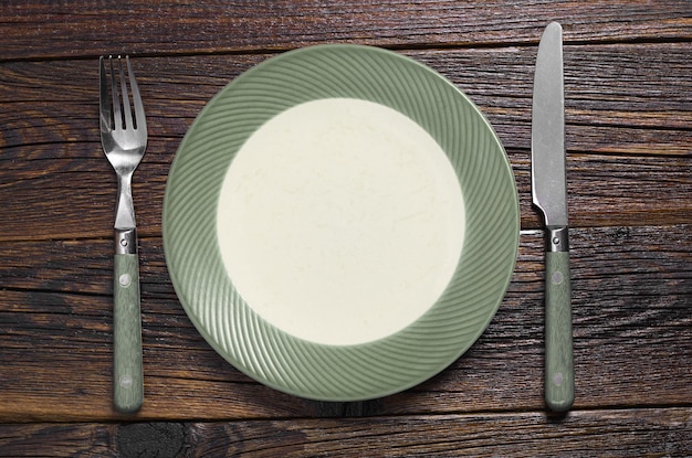 Plato verde vacío con tenedor y cuchillo en la vista superior de la mesa de madera vieja