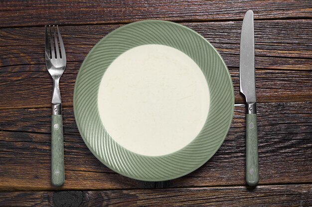 Plato verde vacío con tenedor y cuchillo en la vista superior de la mesa de madera vieja