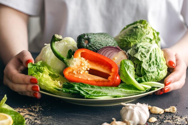 Un plato con verduras frescas en manos femeninas en el primer plano de la cocina