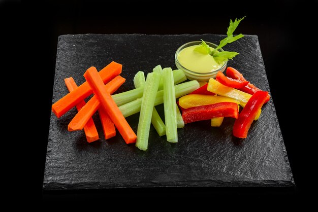 Plato de verduras frescas variadas con salsa de yogur, sobre un fondo negro