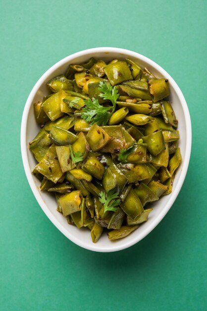 Plato de verduras fritas llamado Flat Green Beans con especias, servido en un cuenco de cerámica, sobre fondo cambiante. enfoque selectivo