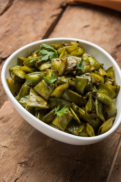 Plato de verduras fritas llamado Flat Green Beans con especias, servido en un cuenco de cerámica, sobre fondo cambiante. enfoque selectivo