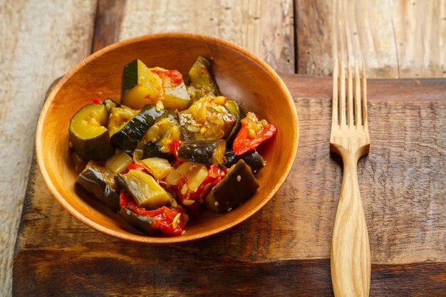 Un plato de verduras a la parrilla en una mesa de madera sobre una tabla de madera junto a un tenedor