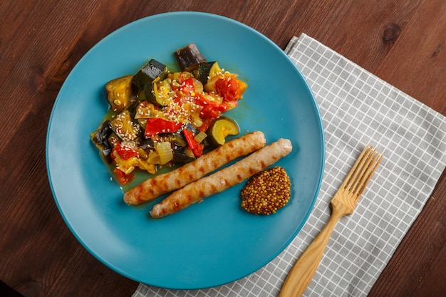 Un plato de verduras con salchichas a la parrilla en una mesa sobre una servilleta de lino y un tenedor de madera