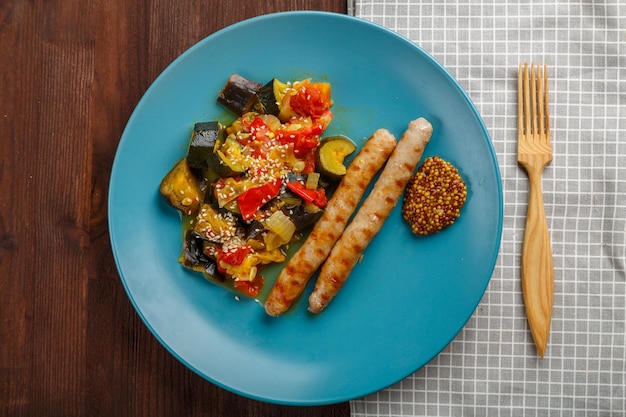 Un plato de verduras con salchichas a la parrilla sobre una mesa en una servilleta y un tenedor de madera
