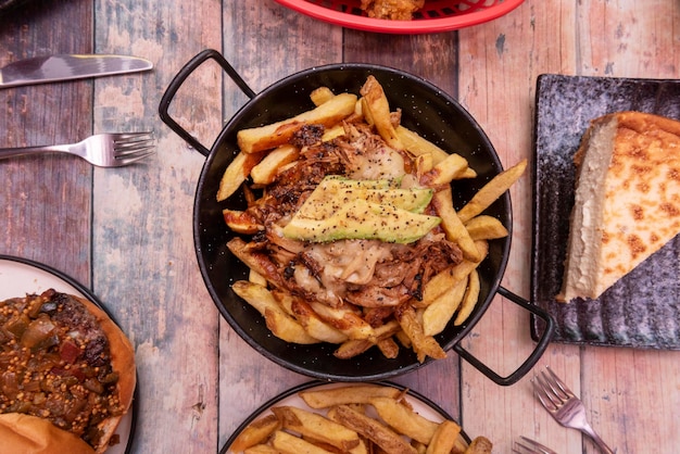 Unos platos de 3 comida rápida latina con carne deshebrada sobre chips con queso y aguacate