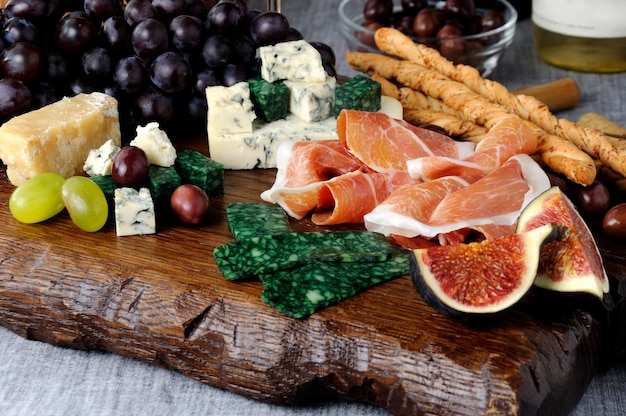 Platos para Antipasto en una tabla de madera con jamón, diferentes tipos de queso, uvas e higos.