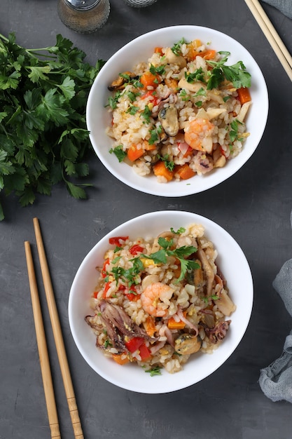 Platos de arroz frito con mariscos, verduras, jengibre y perejil sobre fondo oscuro