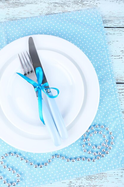 Platos blancos, tenedor, cuchillo y decoración navideña en servilleta de lunares azul sobre fondo de madera