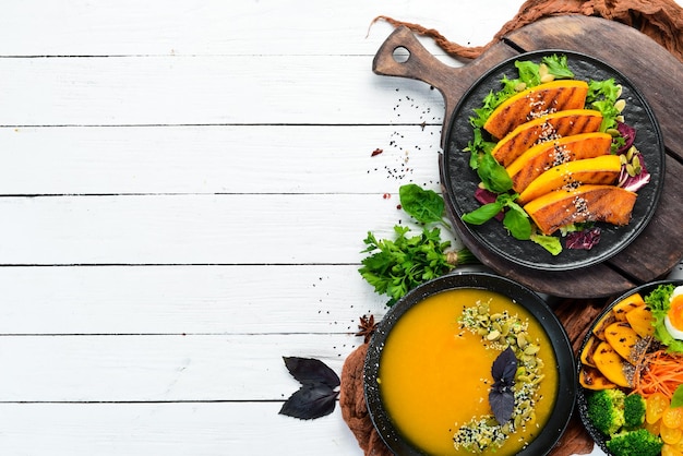 Platos de calabaza en plato negro sobre fondo blanco de madera Platos de otoño Vista superior Espacio libre para su texto