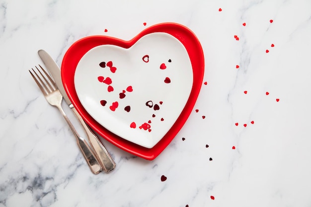 Platos de cena rojos y blancos del día de san valentín con confeti en forma de corazón