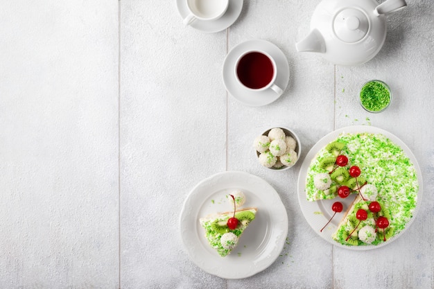 Platos con delicioso pastel de raffaello con hojuelas de coco verde y una taza de té en la mesa de madera blanca