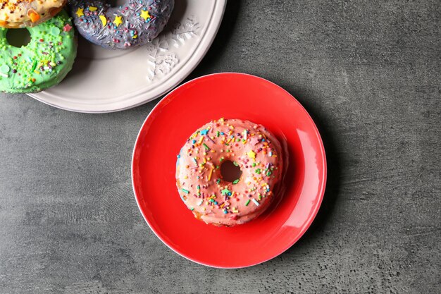 Platos con deliciosos donuts coloridos sobre fondo gris