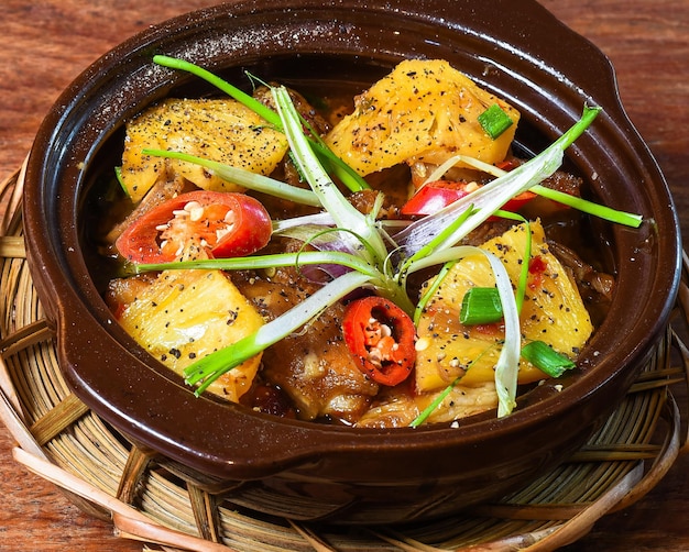 Platos estofados vietnamitas con carne de cerdo y piña con verduras en mesa de madera