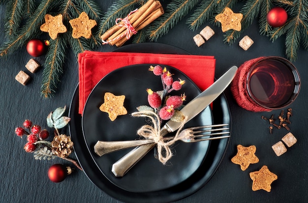 Platos negros y cubiertos vintage con adornos navideños.