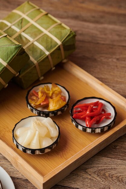 Platos pequeños con ají en escabeche, papaya y ajo en una bandeja con pasteles de arroz pegajoso cocidos para l...