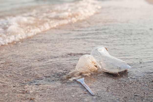 Foto platos de plástico y una bolsa de plástico en el fondo de una playa de arena.