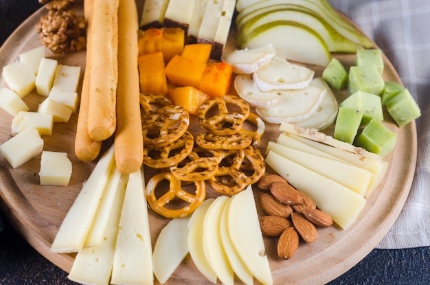 Platos de queso servidos con mermelada de uva, bocadillos, galletas y nueces en una tabla de madera