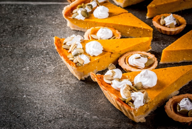 Platos tradicionales de otoño. Halloween, Acción de Gracias. Conjunto de pastel de calabaza picante y tartaletas de calabaza con crema batida y semillas de calabaza en la mesa de piedra negra. copyspace