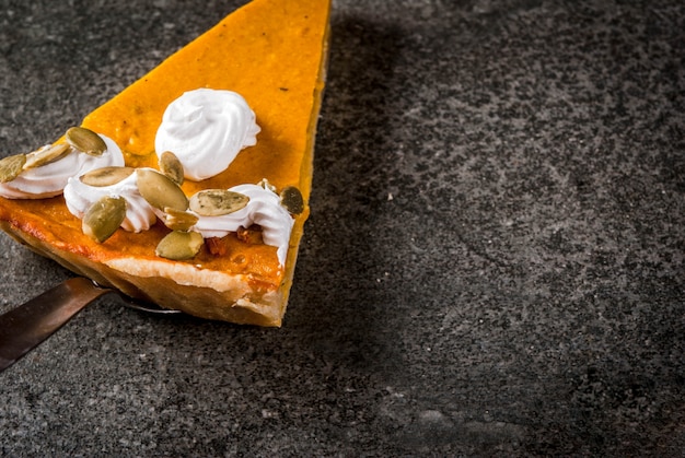 Platos tradicionales de otoño. Halloween, Acción de Gracias. Una pieza de pastel de calabaza picante con crema batida y semillas de calabaza en la mesa de piedra negra. copyspace