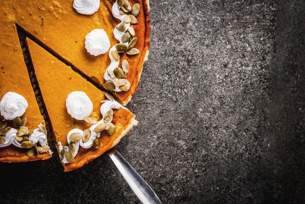 Platos tradicionales de otoño. Halloween, Acción de Gracias. Rodajas de pastel de calabaza picante con crema batida y semillas de calabaza en la mesa de piedra negra. Vista superior copyspace