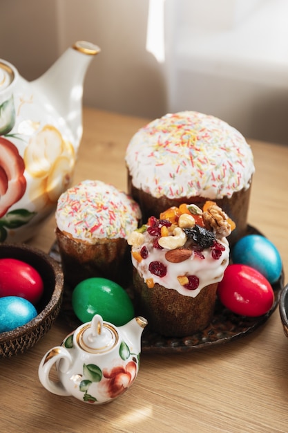 Foto platos con tres pasteles de pascua ortodoxos tradicionales y huevos pintados de rojo, verde y azul, y teteras de flores vintage