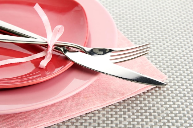 Platos vacíos rosados con tenedor y cuchillo sobre un mantel gris