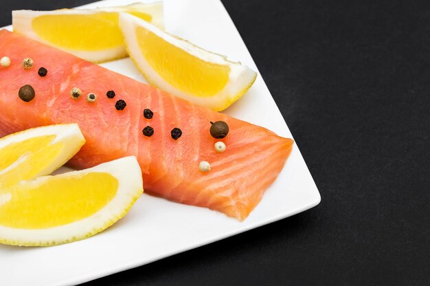 Platte mit Filet vom roten Fisch, Zitronenscheiben und Gewürzen auf schwarzem Hintergrund
