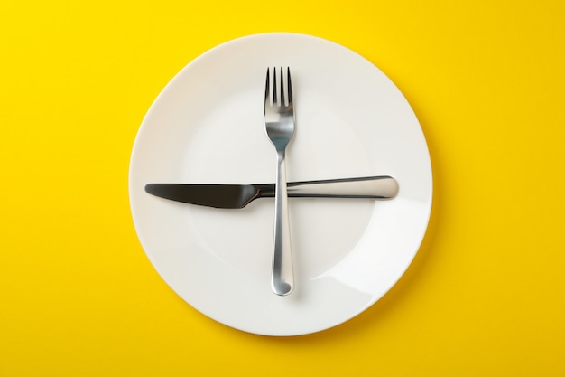 Platte mit Gabel und Messer auf gelbem Hintergrund, Draufsicht