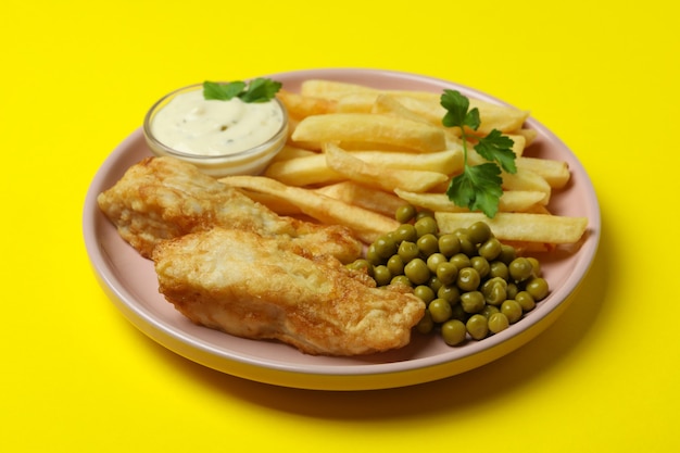 Platte mit gebratenem Fisch und Pommes auf gelb isoliert