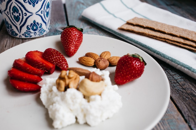 Platte mit Hüttenkäse, Erdbeeren und Nüssen, einem Tasse Kaffee und Tüchern auf Holztisch, gesundes Lebensmittel, Frühstück