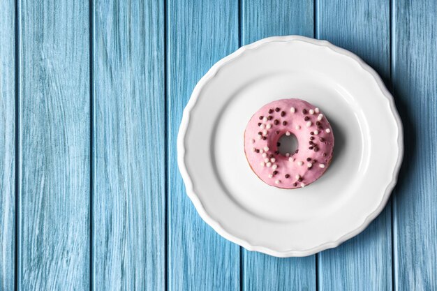 Platte mit köstlichem Donut auf blauem Holzhintergrund