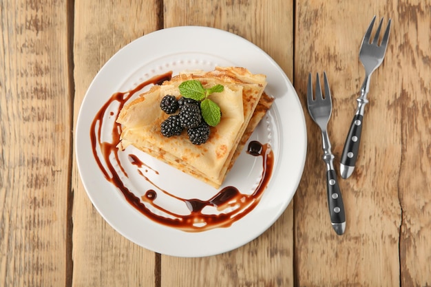 Platte mit köstlichen dünnen Pfannkuchen und Beeren auf Holztisch